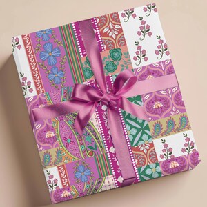 Puede incluir: Una caja de regalo rosa con una cinta rosa y un diseño de patchwork con motivos florales y paisley en tonos rosa, verde y morado.