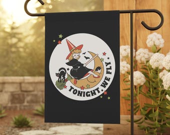 Pode incluir: Bandeira de jardim preta com uma ilustração retrô de uma bruxa montada em uma lua crescente, um gato preto e o texto "TONIGHT WE FLY". A bruxa usa um vestido preto e um chapéu vermelho. Estrelas verdes e amarelas cercam a lua.