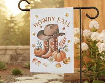 May include: A white garden flag with the words "HOWDY FALL" in brown. The flag features a cowboy hat, boots, pumpkins, and fall foliage. The flag is displayed on a black metal stand in a garden setting.