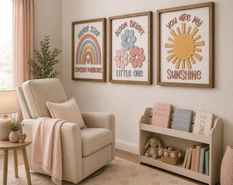 Könnte beinhalten: Drei gerahmte Wandbilder mit Holzrahmen. Das erste zeigt einen Regenbogen und den Text Never Stop Chasing Rainbows. Das zweite zeigt drei Blumen und den Text Bloom Bright Little One. Das dritte zeigt eine Sonne und den Text You Are My Sunshine.