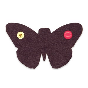 May include: A dark purple leather butterfly with a gold button on the left wing and a red button on the right wing.