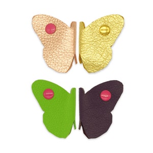 May include: Two pairs of leather butterfly-shaped embellishments. One pair is gold and pink, the other is green and purple.