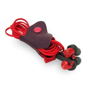 May include: Red and black earphones with a purple leather cord holder. The holder has a pink button.