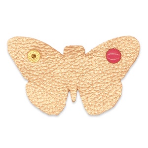 May include: A gold leather butterfly with a red button on one wing and a gold button on the other wing.