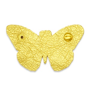 May include: A gold-colored leather butterfly with a metallic finish. The butterfly has two small metal rivets on the wings.