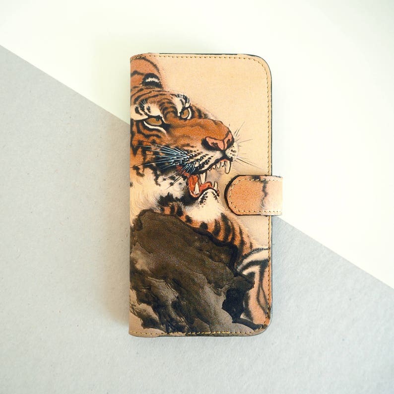 K&ouml;nnte beinhalten: Eine braune Leder-Handyh&uuml;lle mit einer detaillierten Illustration eines Tigers mit offenem Maul. Der Tiger ist in einem traditionellen japanischen Stil dargestellt.