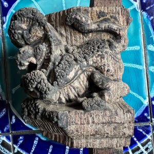 Può includere: Scultura in legno intagliato e dettagliato, dall'aspetto invecchiato. La scultura presenta una creatura stilizzata, possibilmente mitica, con dettagli strutturati e accenti scuri. Il pezzo è montato su una base di legno, mostrando l'intricata maestria artigianale e l'estetica invecchiata.