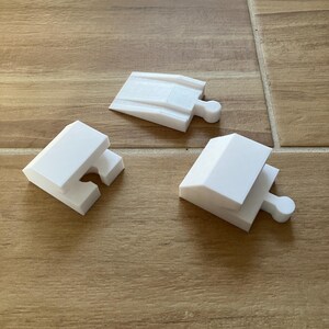 Könnte beinhalten: Drei weiße Plastikteile für ein Modelleisenbahnset. Zwei Teile sind gerade Gleisabschnitte und ein Teil ist ein gebogener Gleisabschnitt.