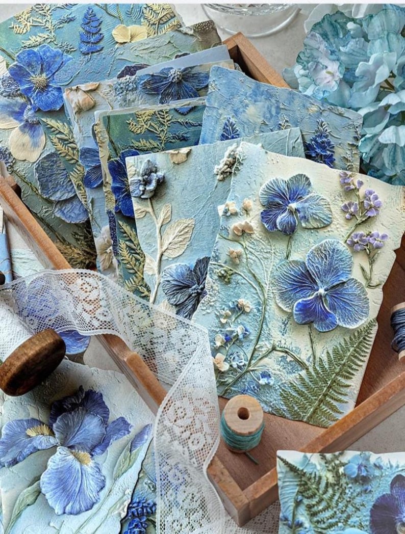 May include: A collection of rectangular cards featuring raised, textured blue and white floral relief designs. Each card displays detailed botanical elements including pressed-style flowers, ferns, and leaves in shades of blue, cream, and green.