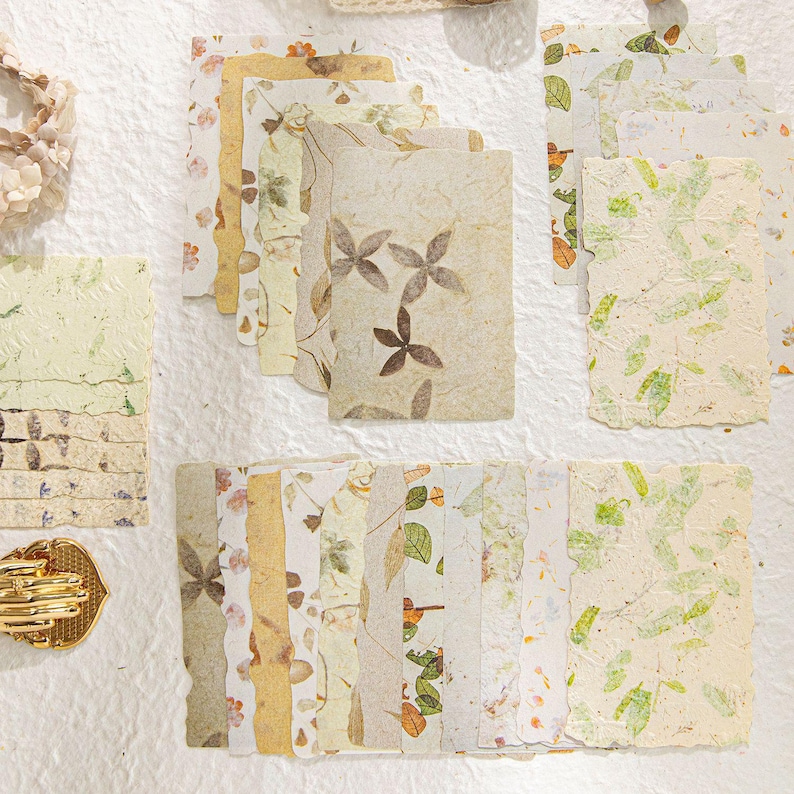 May include: A collection of handmade paper sheets with botanical designs. The papers feature pressed leaves, flowers, and other natural elements in shades of green, brown, and cream. Some sheets have deckled edges, adding a rustic touch.