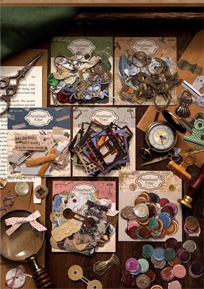 May include: A collection of vintage-style craft supplies, including paper ephemera, decorative seals, and small metal embellishments. The items are arranged on a wooden surface, with the words "Handmade Time" visible on several cards. A magnifying glass and scissors are also present.