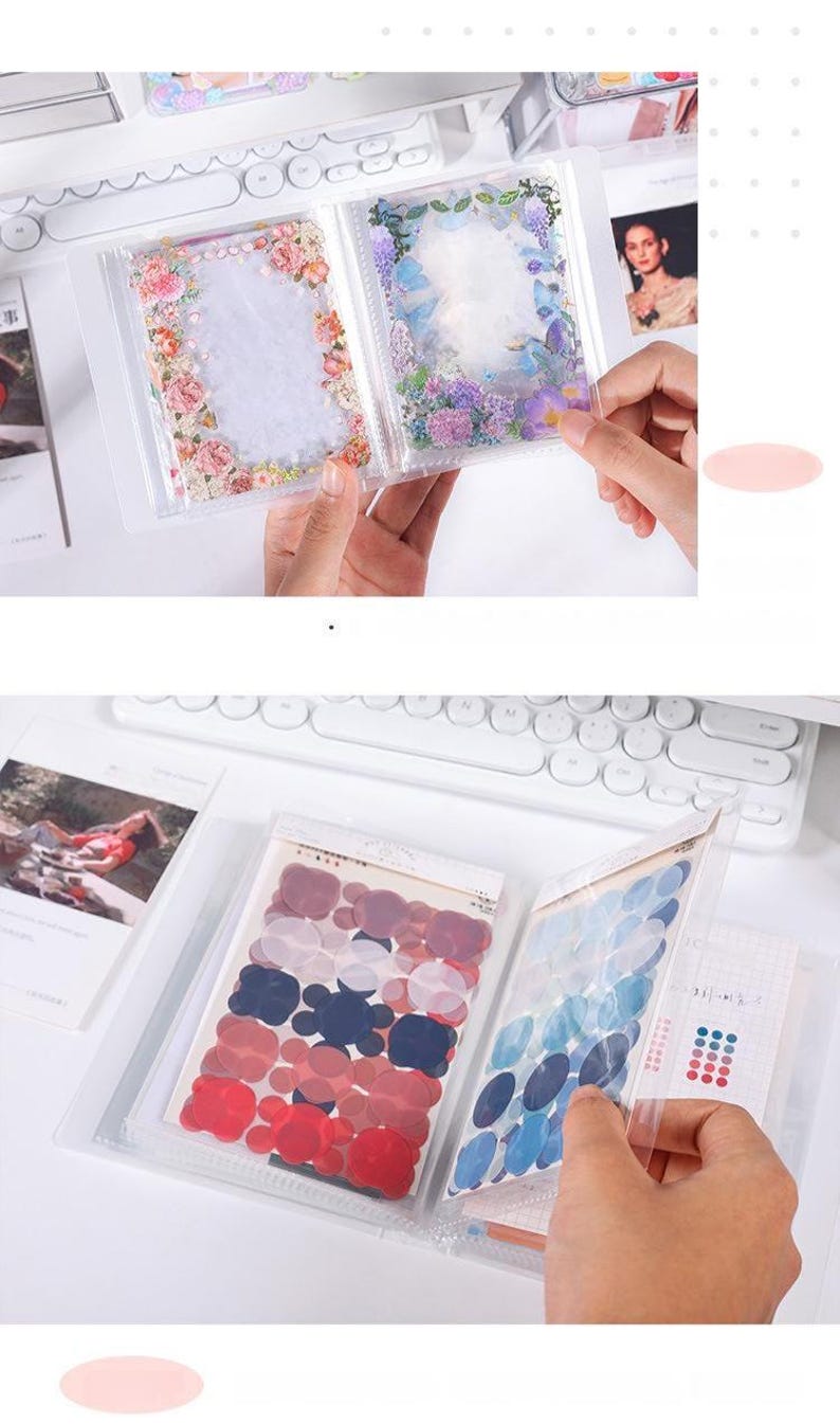 May include: Clear plastic sticker albums with floral and abstract designs. The albums contain stickers in various shapes and colors, including red, blue, and purple. The background includes a white keyboard and other stationery items.
