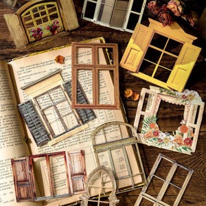 Puede incluir: Surtido de recortes de ventanas y puertas en miniatura en varios estilos y colores, incluyendo amarillo, marrón y blanco. Algunos presentan detalles florales y están dispuestos sobre una página de libro vintage.