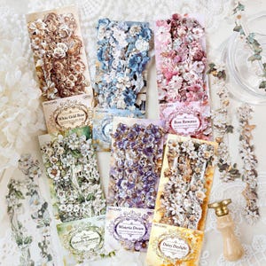 May include: A selection of floral stickers in shades of white, gold, blue, pink, and purple. The packs are labelled with names like "White Gold Rose" and "Rose Romance". The stickers are designed with detailed floral arrangements.