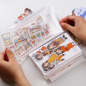 May include: A collection of decorative stickers featuring cartoon illustrations of people, furniture, and scenes. The stickers are packaged in clear plastic sleeves. The text "AMA FAC QUOD VIS DO WHAT YOU LIKE" is visible on one of the packages.