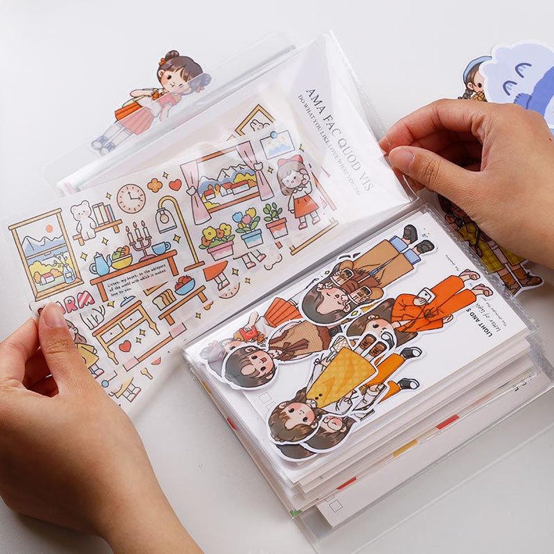 May include: A collection of decorative stickers featuring cartoon illustrations of people, furniture, and scenes. The stickers are packaged in clear plastic sleeves. The text "AMA FAC QUOD VIS DO WHAT YOU LIKE" is visible on one of the packages.