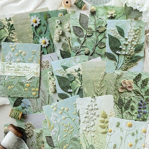 May include: A collection of rectangular cards featuring embossed botanical illustrations in shades of sage, olive, and mint green. The cards display various flowers and plants, including daisies and lilies, with the text Flower And Plant Love Letter Series.