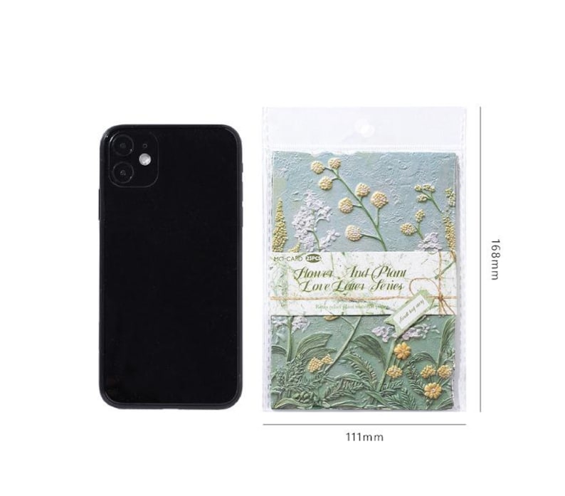 May include: A black smartphone next to a clear plastic package containing stationery cards from the Flower And Plant Love Letter Series. The cards feature embossed floral and botanical designs in shades of green and yellow, measuring 168mm by 111mm.