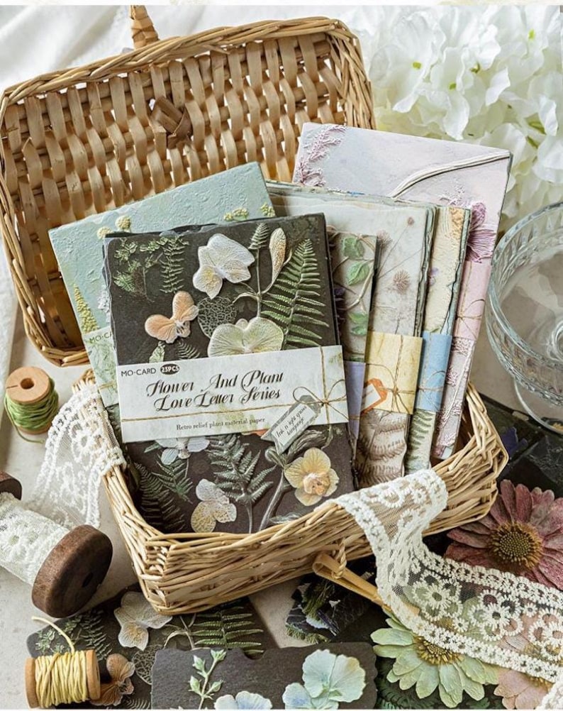 May include: A collection of rectangular paper cards from the Flower And Plant Love Letter Series, featuring embossed botanical and butterfly designs in various colours. The cards are bundled with paper bands and stored in a woven wicker basket.