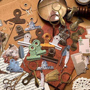 Może przedstawiać: Kolekcja artykułów papierniczych w stylu vintage, w tym spinacze do papieru, lupy i ozdobne kawałki papieru. Klipsy występują w różnych kolorach i wzorach, z ciepłą, ziemistą paletą kolorów.