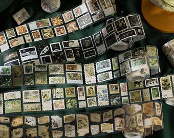 Pode incluir: Vários rolos de fita adesiva decorativa washi com designs de selos postais vintage. Os selos apresentam várias ilustrações, incluindo cogumelos, corpos celestes e elementos botânicos. A fita é em tons de castanho, verde e preto.