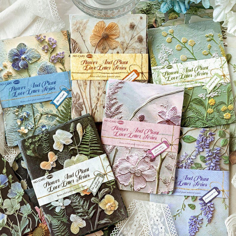 May include: A collection of rectangular paper packs labelled Flower And Plant Love Letter Series, featuring embossed floral and botanical designs in various colours including blue, green, pink, and black, with each pack wrapped in a paper band.