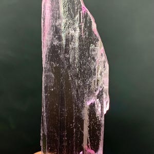 Pu&ograve; includere: Un cristallo rosa traslucido con una punta appuntita e striature su tutta la superficie. Il cristallo &egrave; tenuto in una mano.