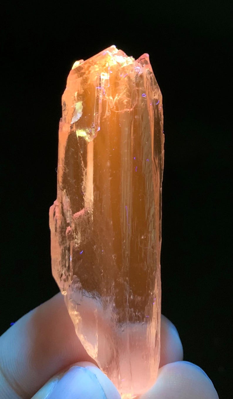 Pu&ograve; includere: Un cristallo translucido di colore arancio-rosa con una forma rettangolare allungata. Il cristallo ha una superficie liscia e lucida ed &egrave; leggermente translucido.