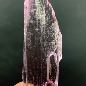 Pu&ograve; includere: Un cristallo rosa traslucido con una punta appuntita e una superficie ruvida e testurizzata.