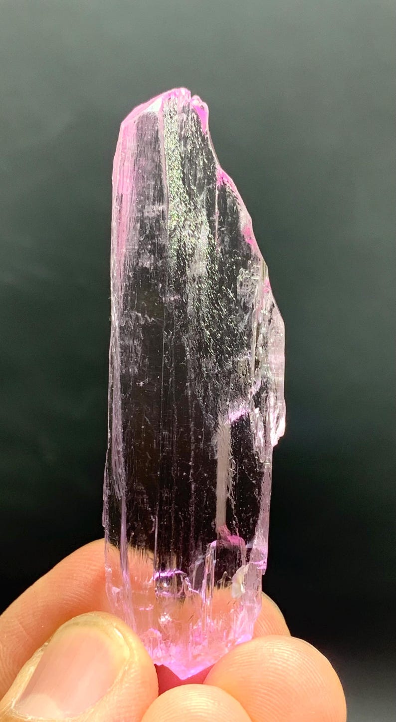 Pu&ograve; includere: Un cristallo rosa traslucido con una punta appuntita e una superficie ruvida e testurizzata.