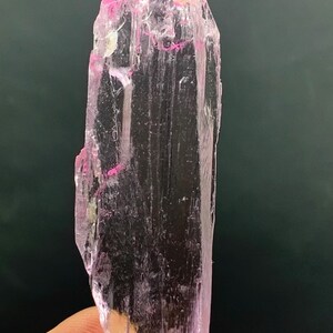 Pu&ograve; includere: Un cristallo allungato trasparente e rosa con striature. Il cristallo &egrave; traslucido e ha una leggera sfumatura rosa.