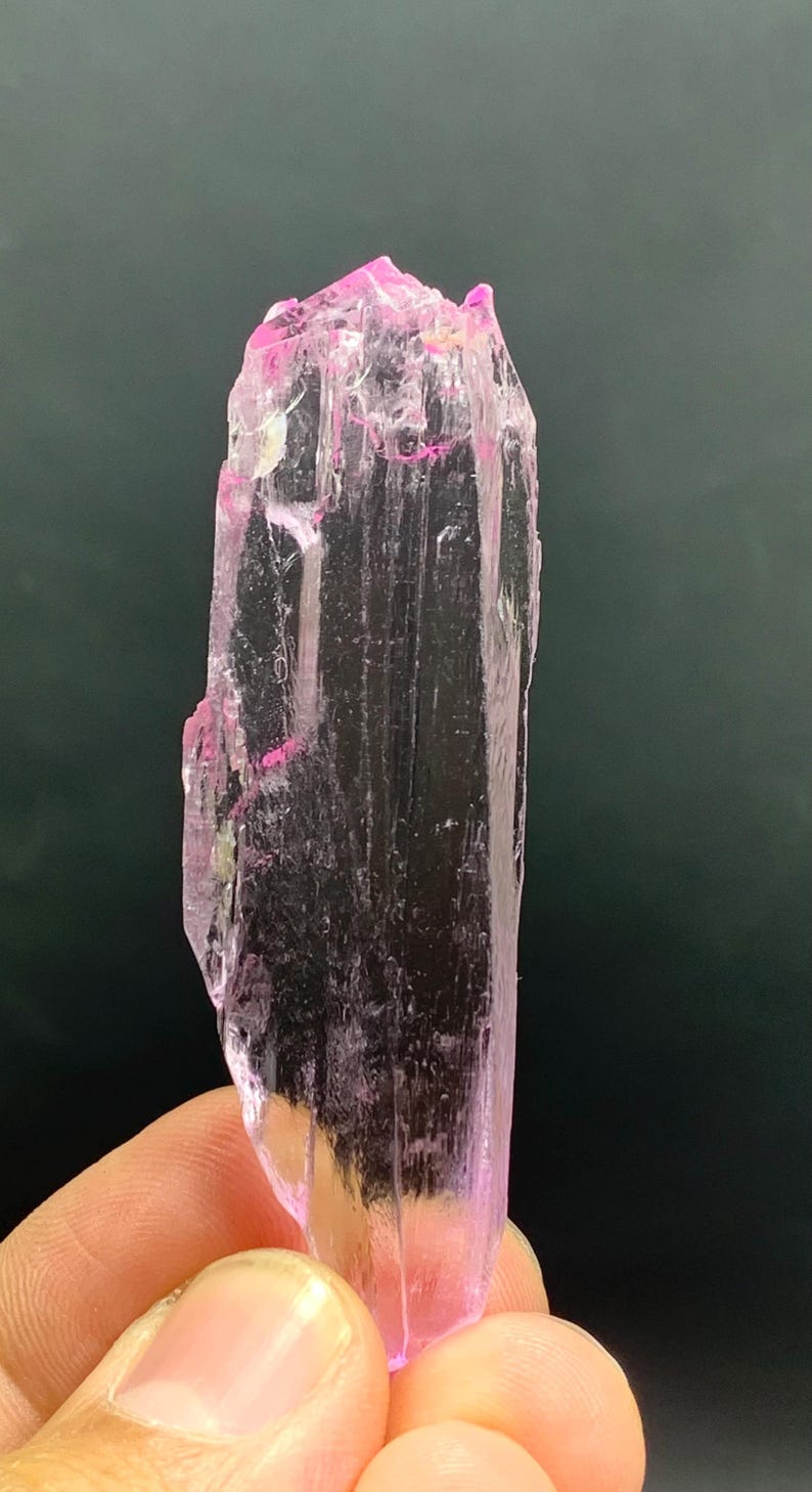 Pu&ograve; includere: Un cristallo allungato trasparente e rosa con striature. Il cristallo &egrave; traslucido e ha una leggera sfumatura rosa.