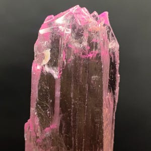 Pu&ograve; includere: Un cristallo rosa, traslucido, sfaccettato con una punta appuntita. Il cristallo &egrave; trasparente e ha una leggera sfumatura rosa.