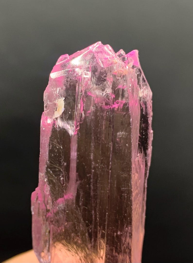 Pu&ograve; includere: Un cristallo rosa, traslucido, sfaccettato con una punta appuntita. Il cristallo &egrave; trasparente e ha una leggera sfumatura rosa.