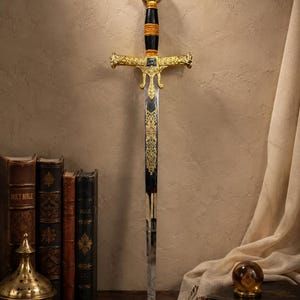 以下が含まれることがあります： 磨き上げられたスチール製の刃に複雑な金色のフィリグリー彫刻が施された装飾用の剣。柄には金色のアクセントが入った黒いグリップ、精巧な金色のクロスガード、中央にエンブレムが付いた円形のポメルが備わっています。