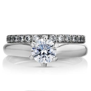 May include: A silver engagement ring set with a large, round, brilliant-cut diamond centre stone and a matching band of smaller diamonds.