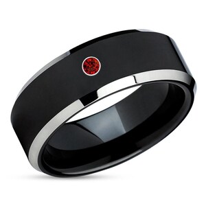 May include: A black tungsten carbide ring with a silver band and a single red gemstone.