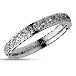 May include: A silver titanium band with a row of small, clear cubic zirconia stones set in the band. The band is engraved with the word "TITANIUM".