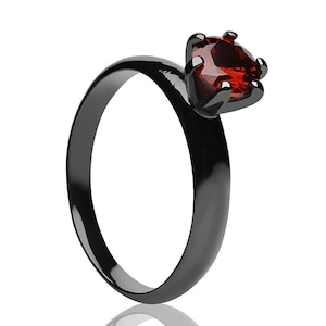 May include: A black ring with a red heart-shaped gemstone.