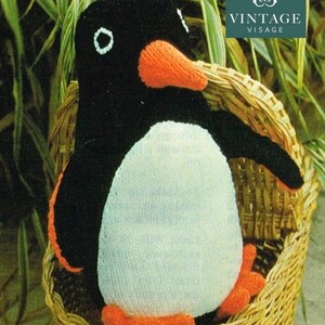 Può includere: Un pinguino fatto a mano all'uncinetto con pancia bianca, corpo nero e becco e piedi arancioni, seduto in un cestino di vimini. Il pinguino ha dettagli bianchi sugli occhi. L'immagine include il testo "VINTAGE VISAGE".