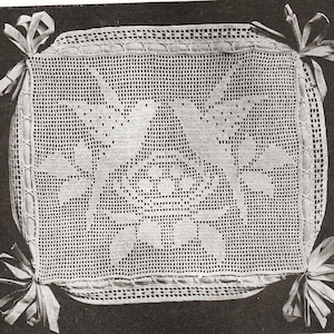 May include: A square, off-white crocheted doily with a floral design in the center. The doily is trimmed with a ribbon and tied at each corner with a bow. The crochet work is detailed and intricate.