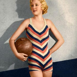 May include: A vintage-style swimsuit with a chevron pattern in red, navy, and cream colors. The one-piece suit has a scoop neck and short shorts. A brown leather ball is held in the person's hand. The image has a retro aesthetic.