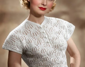 May include: A vintage-style white knit top with a delicate openwork pattern and short sleeves. The top features a button-up front with small, round buttons. The model is wearing a dark bow in her hair and red lipstick.
