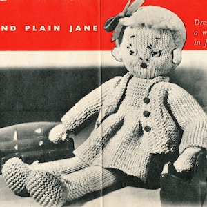 May include: A knitted doll with a round face, wearing a button-down coat and a bow in its hair. The doll is seated, with its legs extended. The doll's features are stitched, and it has a vintage aesthetic. The text "AND PLAIN JANE" is visible in the background.