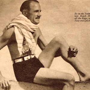 May include: Vintage sepia-toned image of a person wearing black beach shorts with a white belt, seated with a scarf around their neck. The text reads, "Be in the Swim! These new Beach Shorts are all the Rage, and are so Easy and Quick to Knit."