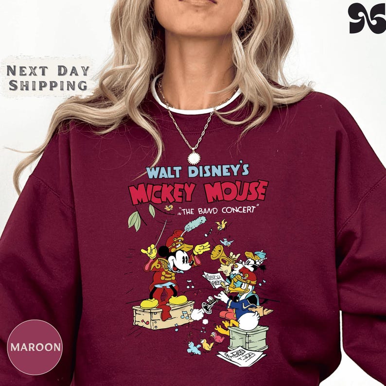 A person wearing a maroon sweater with a graphic design featuring Mickey Mouse and other Disney characters from Walt Disney's "Mickey Mouse" concert.
