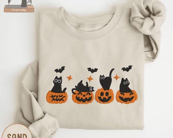 May include: Sand-colored sweatshirt with an embroidered Halloween design. The design features four black cats sitting on orange jack-o'-lanterns, with bats and stars above. The sweatshirt has long sleeves and a crew neck. The word "EMBROIDERY" is at the top left.