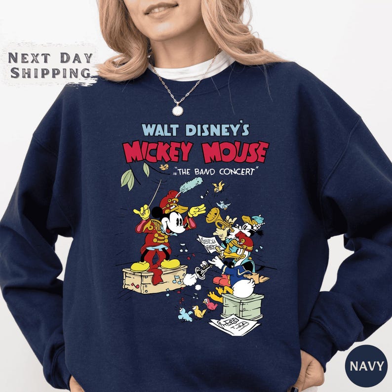 A navy blue sweatshirt with a graphic design featuring Mickey Mouse and other Disney characters, along with the text "Walt Disney's Mickey Mouse" and "The Band Concert".