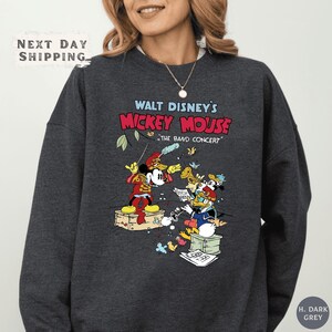 A woman wearing a gray sweatshirt with a colorful graphic of Mickey Mouse and other Disney characters.