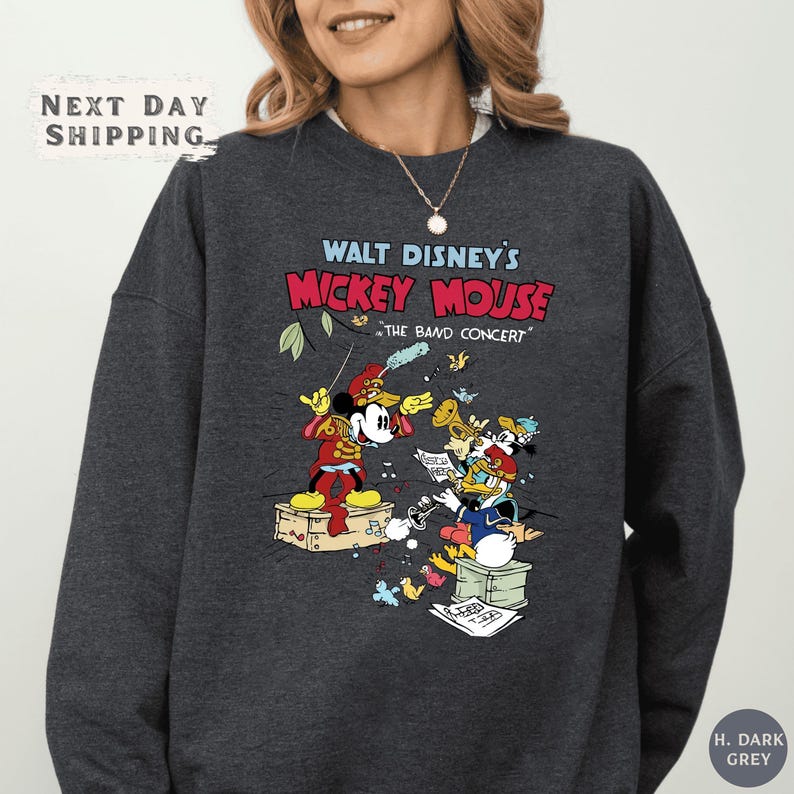A woman wearing a gray sweatshirt with a colorful graphic of Mickey Mouse and other Disney characters.